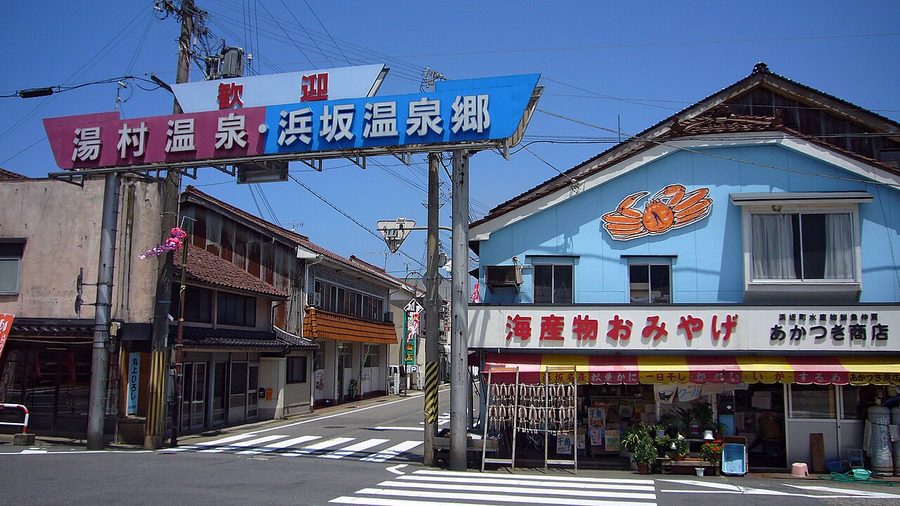「湯村温泉・浜坂温泉郷」と書かれた歓迎ゲートと、蟹の看板を掲げた海産物店が並ぶ通り