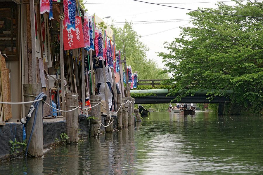 掘割沿いの商店にこいのぼりが掲げられ、奥では川下りの舟が行き交う柳川の風景