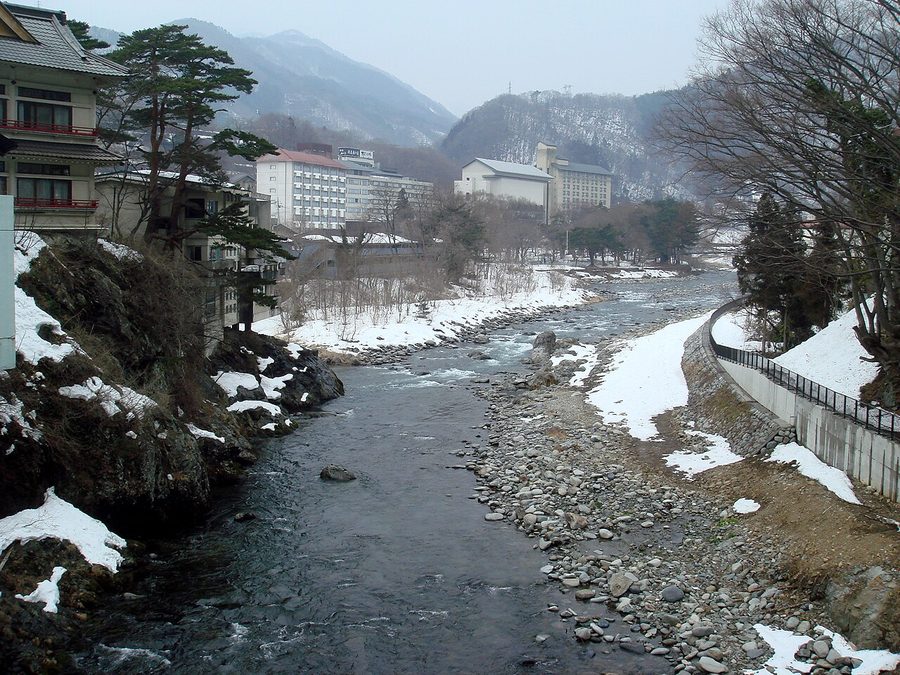 雪の残る川沿いの温泉旅館とみられる建物群